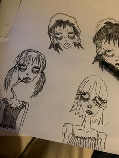 four different faces drawn on paper with a pen in the foreground and another drawing behind them