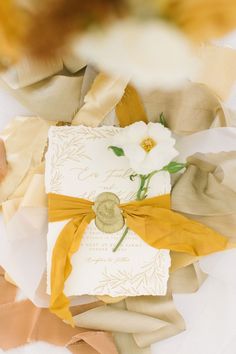 a wedding card with a yellow ribbon tied around it and some flowers on top of it