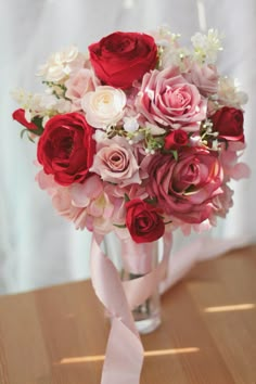 a vase filled with lots of pink and red flowers on top of a wooden table