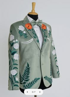 a green suit with white flowers and leaves on the lapel has an orange bow tie