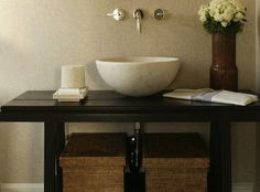 a bathroom sink sitting under a mirror next to a vase with flowers on top of it