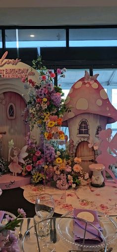 the table is set up for a birthday party with flowers and fairy houses on it