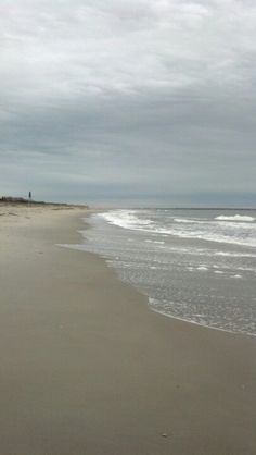 an empty beach with waves coming in to the shore and people walking on the sand