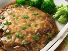 a white plate topped with meat covered in gravy next to broccoli