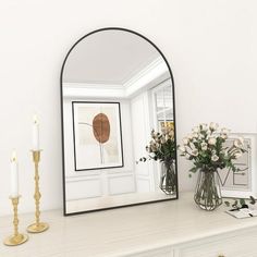 a mirror sitting on top of a dresser next to a vase with flowers in it