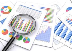 a magnifying glass sitting on top of papers with graphs and pies in it