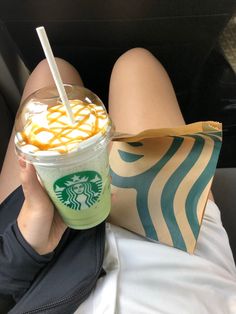 a woman is sitting in the back seat holding a starbucks drink and a paper bag