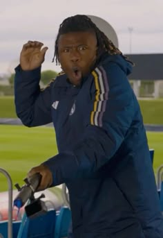 a man with dreadlocks standing in front of a soccer field holding his fist up