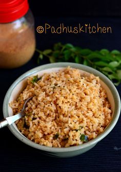 a bowl filled with brown rice next to a jar of seasoning and sprigs