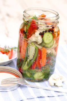 a mason jar filled with pickles, cucumbers, tomatoes and other veggies