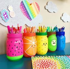 colorful mason jars filled with pencils and markers on a blue table next to a drawing pad