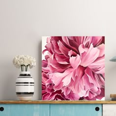 a pink flower is displayed on top of a dresser next to a vase with white flowers