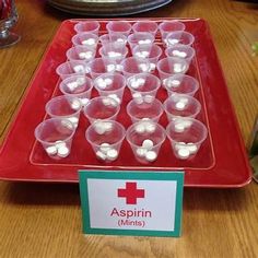 a red tray filled with plastic cups on top of a wooden table next to a sign that says aspiin men