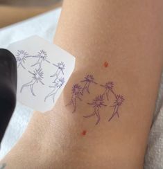 a person with a tattoo on their arm holding up a piece of paper that has dandelions drawn on it