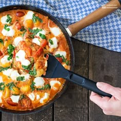 a skillet filled with food on top of a wooden table next to a blue and white checkered cloth