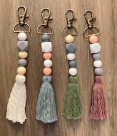 four key chains with tassels and beads hanging from them on a wooden surface