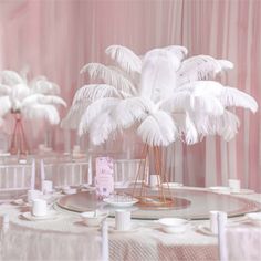 a table topped with lots of white feathers next to a tall vase filled with flowers