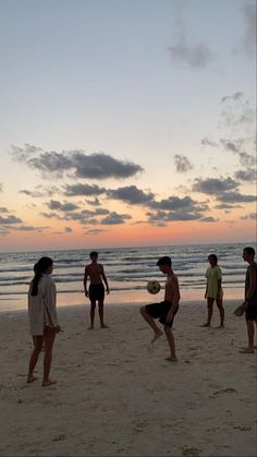 a group of people standing on top of a beach next to the ocean at sunset