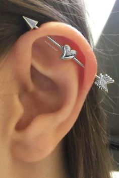 a woman wearing ear piercings with an arrow and heart on the end of her ear