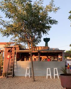 an outdoor bar with two white chairs and a tree in the foreground, next to it