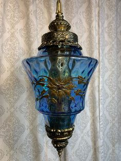 an ornate blue glass lamp hanging from a gold colored ceiling fixture on a white wall