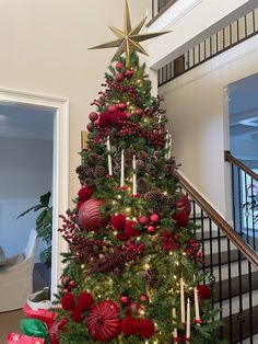 a christmas tree decorated with red balls and pineconis is in front of the stairs