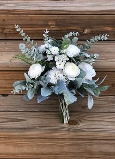 a bouquet of white flowers and greenery on a wooden surface with wood planks