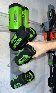 a man is holding two green and black tools in front of a wall mounted tool rack