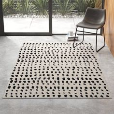 a black chair sitting next to a white rug on top of a cement floor in front of a window