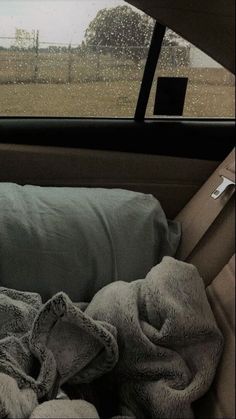 a blanket and pillows in the back seat of a car with rain coming down on it