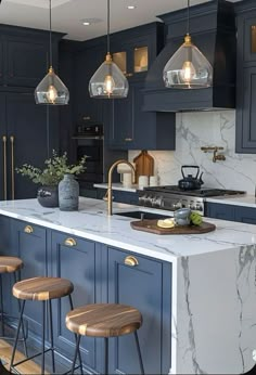 a kitchen with blue cabinets and marble counter tops, gold accents and pendant lights hanging from the ceiling