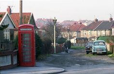 a car parked on the side of a road next to a red phone booth and telephone box