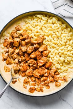 chicken and macaroni in a skillet on a marble counter top with a spoon