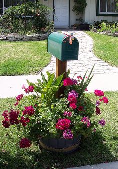 a green mailbox sitting in the middle of a flower pot filled with pink flowers