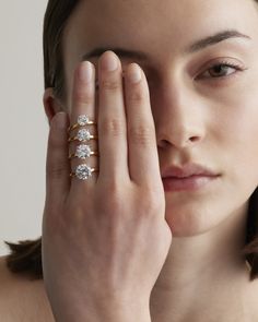 a woman holding her hand up to her face with three diamond rings on each finger