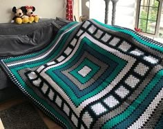 a crocheted blanket is sitting on a couch next to a teddy bear and window