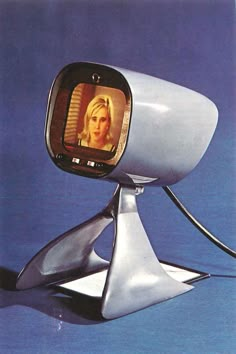 an old television with a woman's face on the screen, sitting in front of a blue background