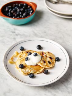 pancakes with blueberries and whipped cream are on a plate next to a bowl of berries