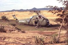 a helicopter is parked on the ground near some trees and bushes in an arid area