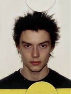 a young man with black hair standing in front of a white wall