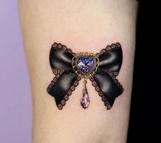 a woman's thigh with a black bow tattoo on her left leg and an amethorate in the center