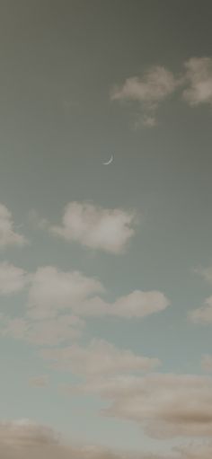 an airplane flying in the sky with a half moon above it and some clouds behind it