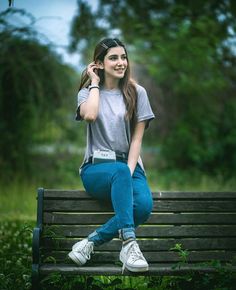 a young woman sitting on top of a wooden bench in the park talking on a cell phone