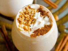 two glasses filled with milk and cinnamon on top of a wooden table next to cinnamon sticks