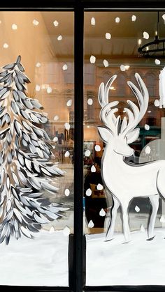 a window decorated with white paper cut out of animals and snowflakes, in front of a christmas tree