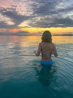 a woman is sitting in the water with her back turned to the camera and looking at the sunset