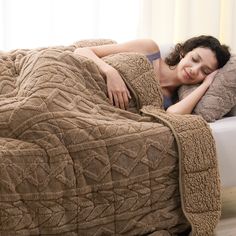 a woman laying on top of a bed covered in a brown blanket and smiling at the camera