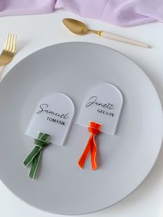 two pieces of paper with name tags on them sitting on a plate next to forks and spoons