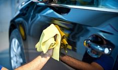 a man wiping down the side of a car with a yellow cloth on it's windshield