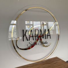 a glass sign that says karma salon studio on the side of a white wall next to a wooden table